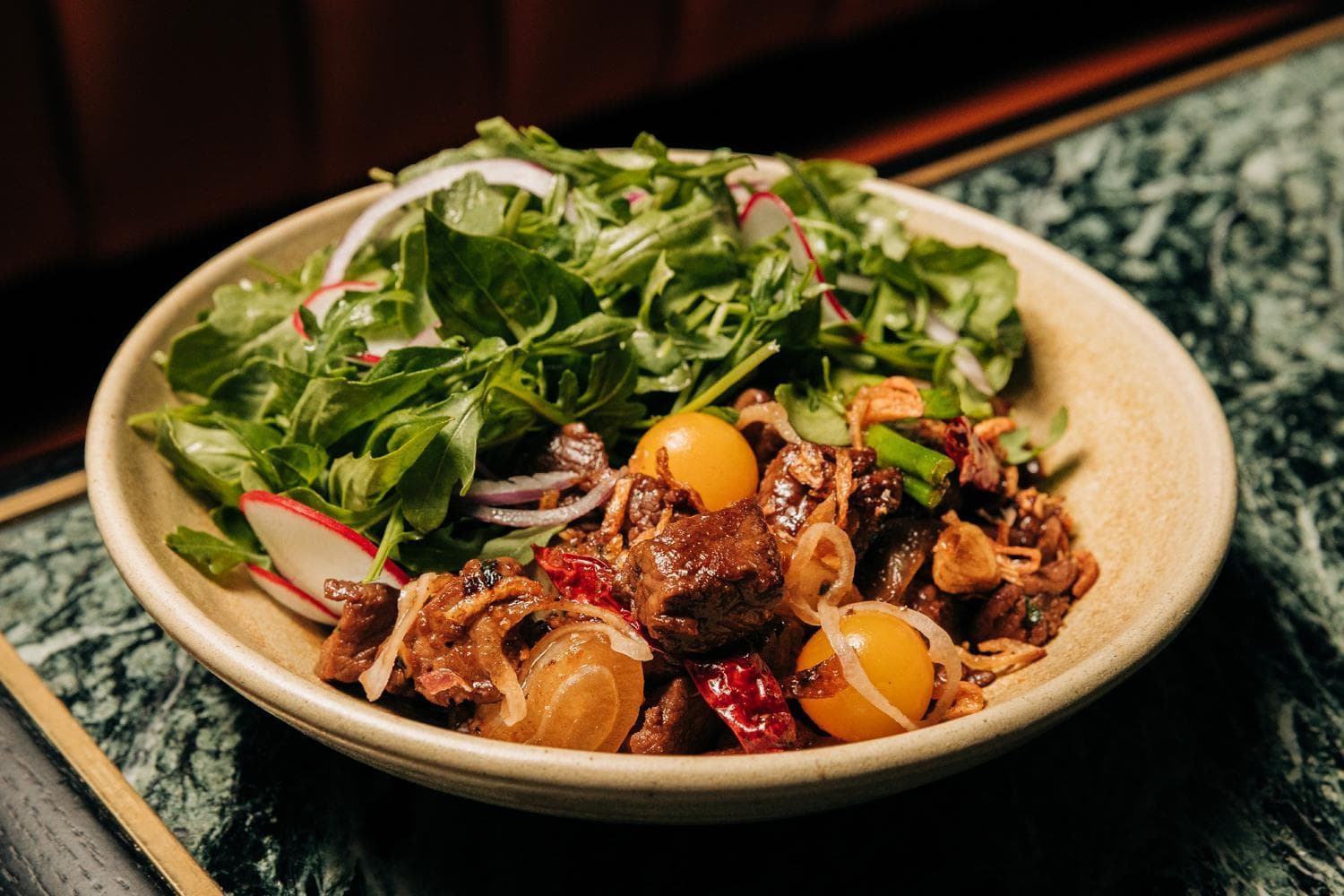A bowl of colorful stir-fry featuring cherry tomatoes, onion slices, cilantro, and assorted vegetables served on a dark plate.