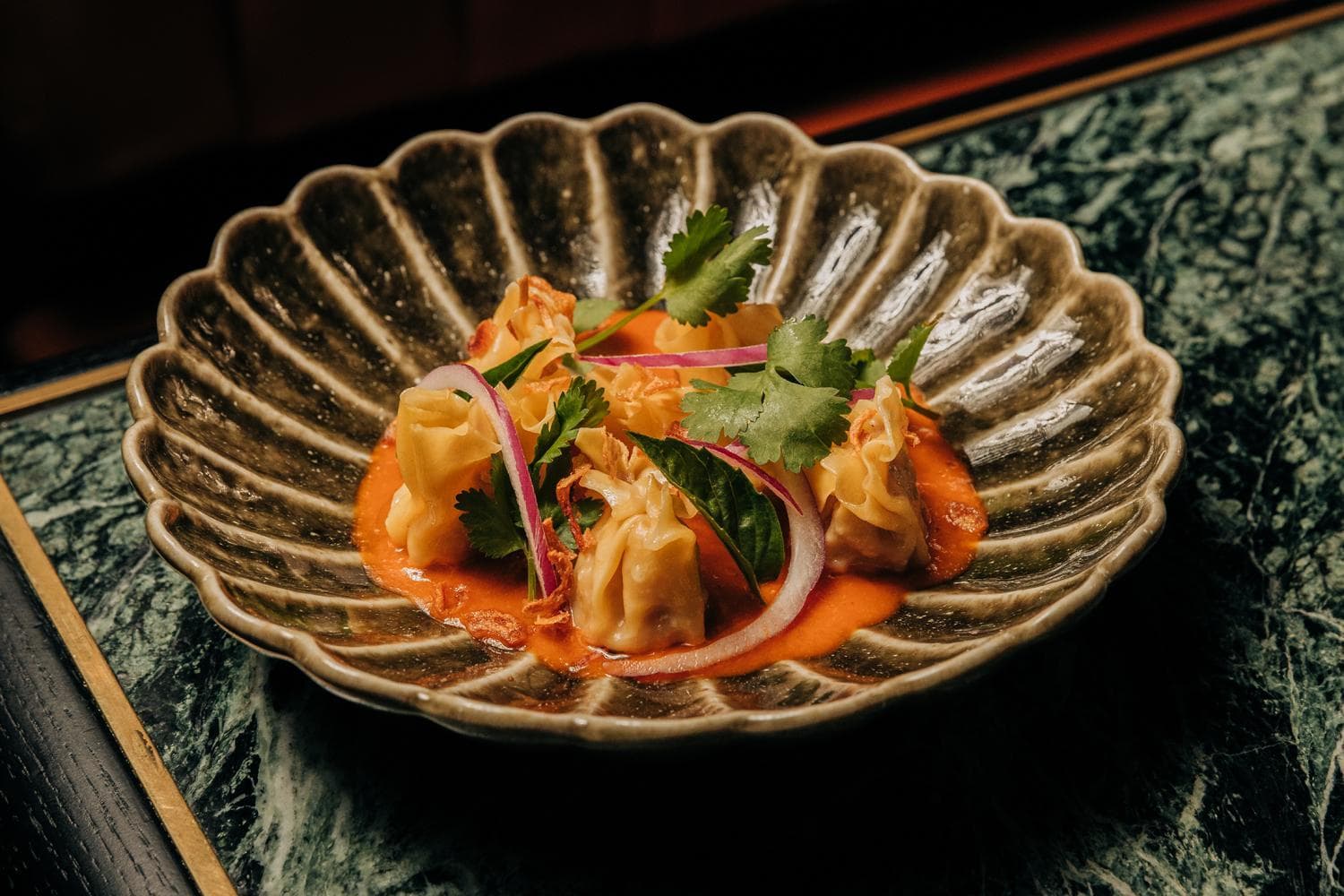 Shrimp and Pork dumplings in a brown bowl with a rice orange sauce and herbs.